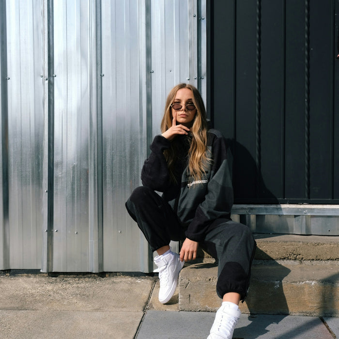 woman in black jacket and white pants sitting on gray concrete floor
