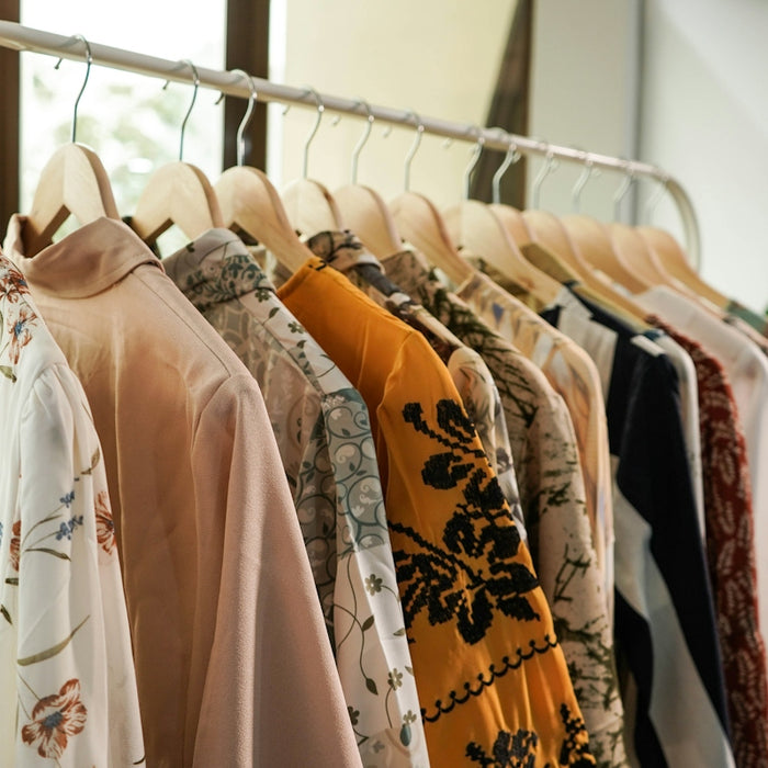 A row of assorted patterned blouses hanging on wooden hangers on a clothing rack