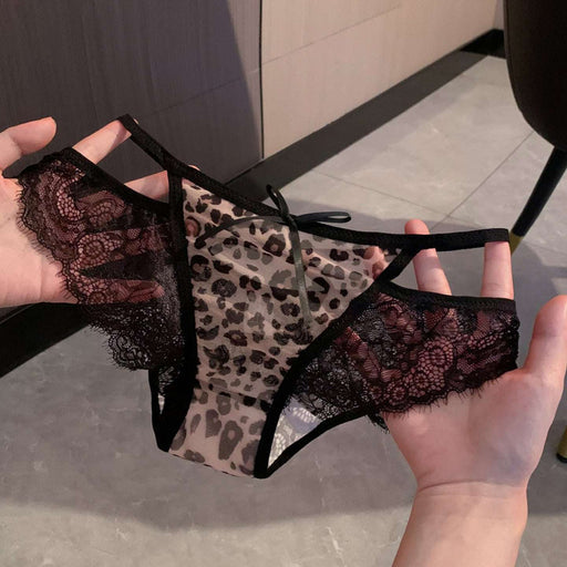 A pair of women's lace panties with a leopard print center panel, held up by two hands against an indoor tiled floor background.