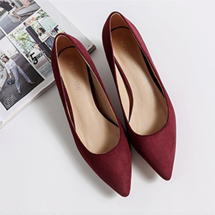 Pair of red pointed-toe shoes on a white surface with a magazine in the background.