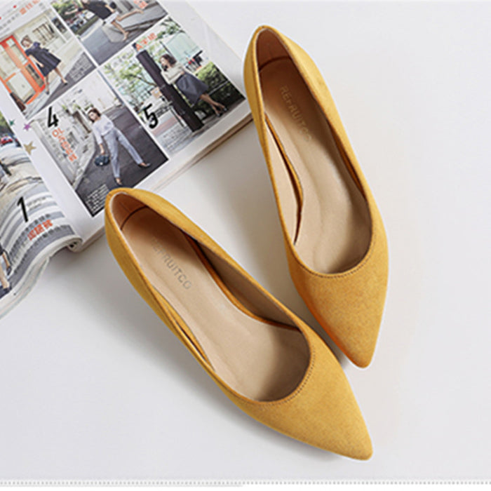 Yellow pointed-toe shoes on a white surface with a magazine in the background