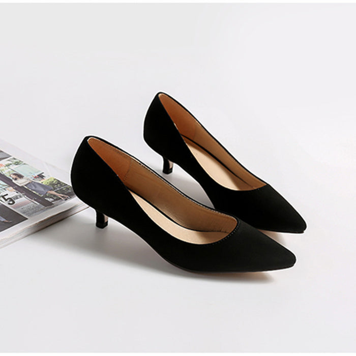 Pair of black high-heeled shoes on a white surface with a magazine in the background.