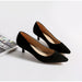 Pair of black high-heeled shoes on a white surface with a magazine in the background.
