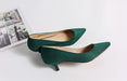 Pair of green high-heeled shoes on a light gray surface with a magazine in the background.