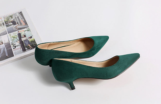 Pair of green high-heeled shoes on a light gray surface with a magazine in the background.