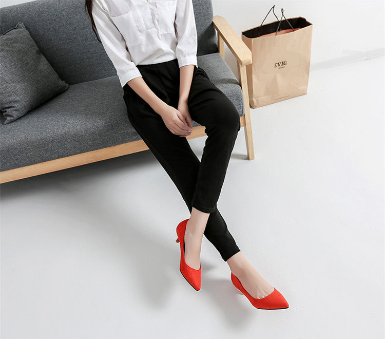 Person sitting on a gray sofa wearing black pants and red shoes, with a beige bag in the background.