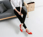 Person sitting on a gray sofa wearing black pants and red shoes, with a beige bag in the background.