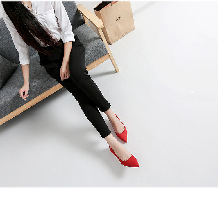Person wearing black pants and red shoes sitting on a gray couch with a white background