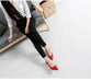 Person wearing black pants and red shoes sitting on a gray couch with a white background