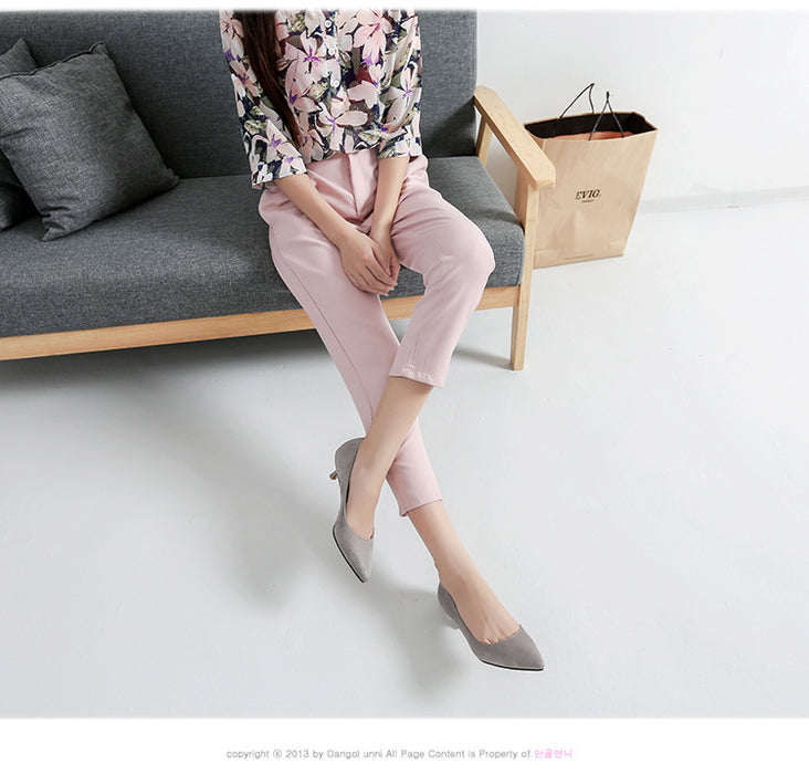 Person sitting on a gray sofa wearing pink pants and gray shoes, with a beige bag on the floor.