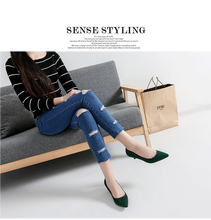 Woman sitting on a gray sofa wearing a striped sweater, ripped jeans, and green shoes, with a beige bag beside her.