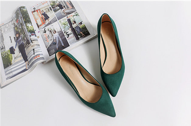 Green high-heeled shoes on a white surface with a magazine in the background