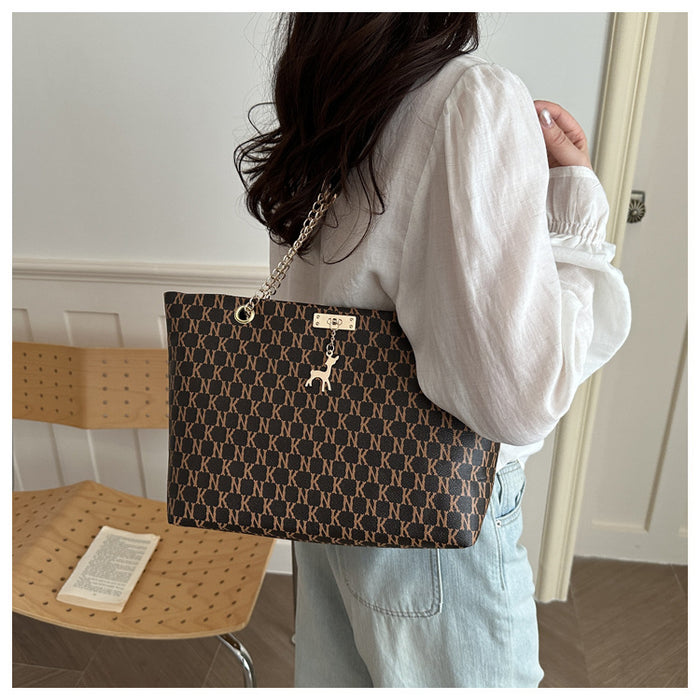 A woman wearing a white long-sleeve blouse and light blue jeans carries a brown tote bag with a beige geometric monogram pattern, gold-tone chain strap, and a small deer emblem on the front.