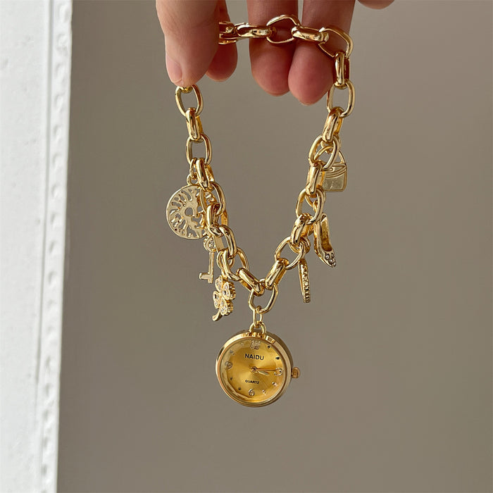 Gold charm bracelet with a watch charm held by a hand against a neutral background