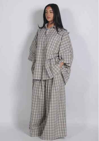A model wearing a matching two-piece lounge set in a beige and gray plaid pattern, featuring a long-sleeve button-up shirt and wide-leg pants, set against a plain light gray background.