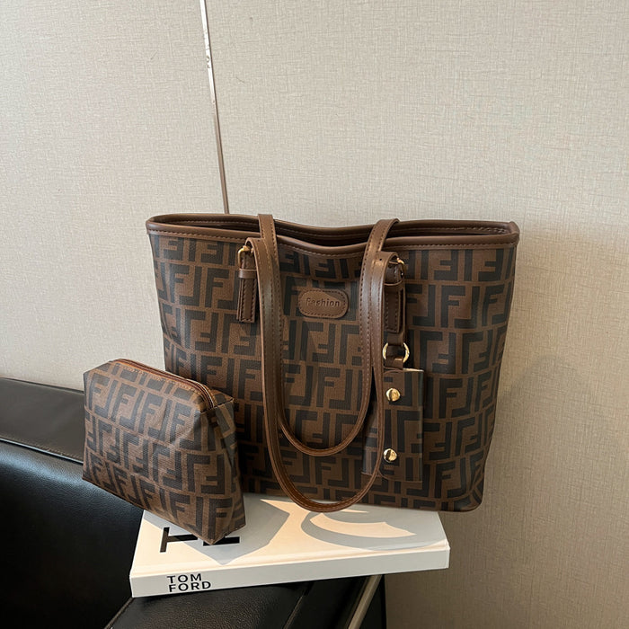 A brown Fendi tote bag with the signature FF monogram pattern and a matching zip pouch, displayed on a white book on a black leather chair against a beige wall.