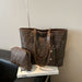 A brown Fendi tote bag with the signature FF monogram pattern and a matching zip pouch, displayed on a white book on a black leather chair against a beige wall.