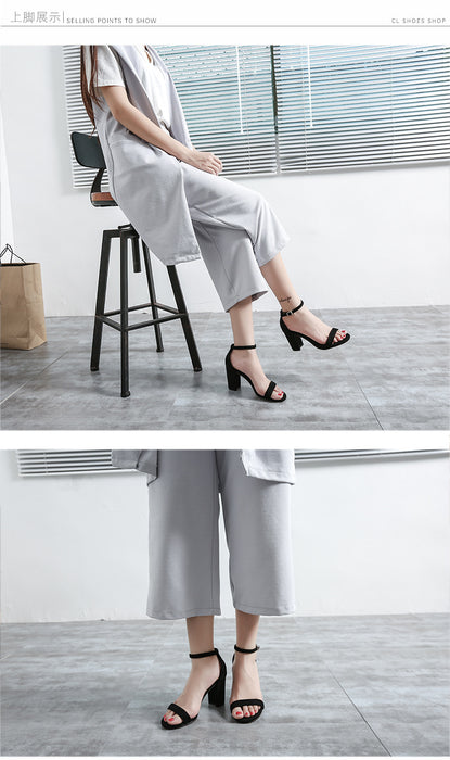 Woman sitting on a stool wearing white pants and black high-heeled sandals in a minimalistic setting.