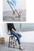 Person sitting on a stool wearing blue jeans and high-heeled shoes in an indoor setting.