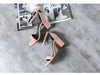 Pair of pink high-heeled shoes on a gray surface with a magazine underneath.