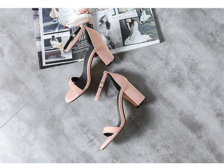 Pair of pink high-heeled shoes on a gray surface with a magazine underneath.