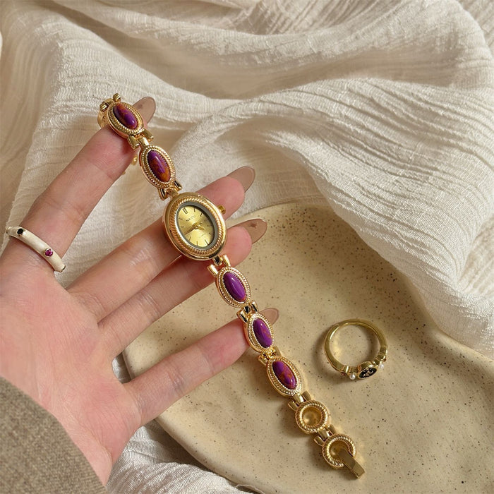 Gold bracelet with purple stones held by a hand on a textured beige surface.