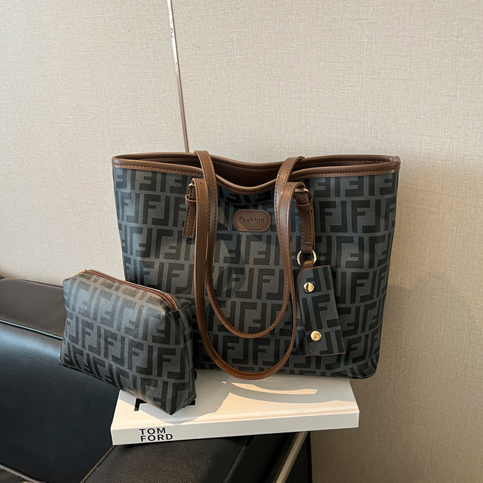 A Fendi tote bag in dark gray and black FF monogram canvas with brown leather trim, displayed on a white book with a matching small pouch beside it.