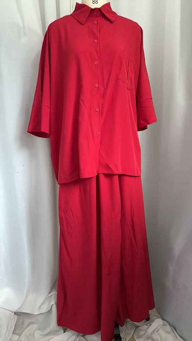 A bright red two-piece clothing set consisting of a short-sleeve button-up shirt and matching wide-leg pants, displayed on a hanger against a white draped fabric backdrop.