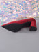 A red suede pointed-toe high heel shown from the side, with a black sole and block heel, placed on a gray surface in front of a shimmering iridescent fabric backdrop.