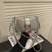 A metallic silver shoulder bag with a chain strap and studded details, held by a hand wearing a black sweater in front of a white slatted wall.