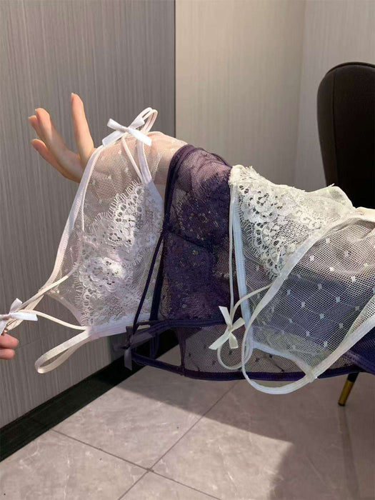 Three sheer lace and mesh lingerie pieces in white, dark purple, and pale blue-green are draped over a person's arm in an indoor setting.