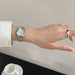 Hand wearing a silver watch with a plain background