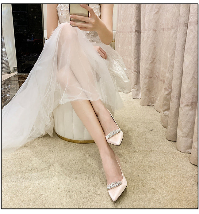 Woman in a white dress with sparkling shoes sitting on a chair.