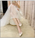 Woman in a white dress with sparkling shoes sitting on a chair.