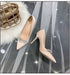 Beige high-heeled shoes with crystal embellishments on a gray surface with a decorative bag.