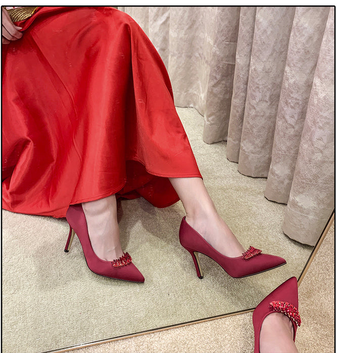 Red high-heeled shoes with decorative elements worn by a person sitting on a reflective surface.