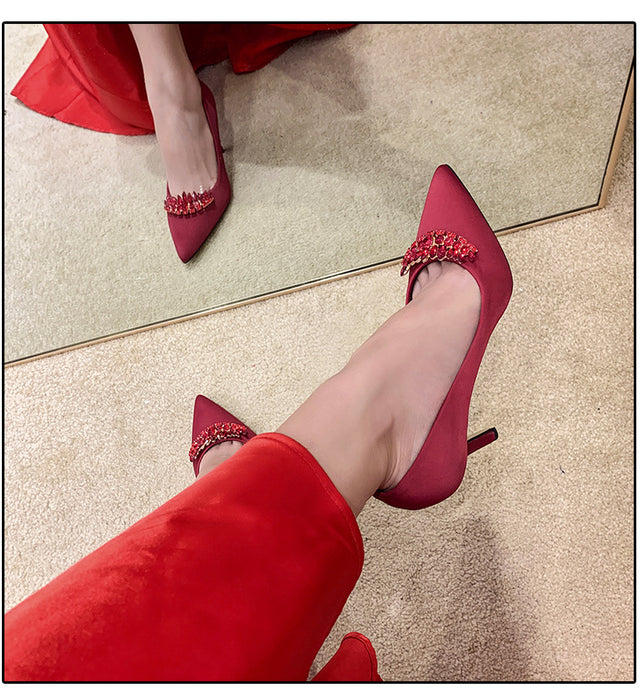 Red high-heeled shoes with embellishments worn by a person in red pants on a light-colored floor.