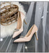 Pair of beige high-heeled shoes with crystal embellishments on a gray surface with a decorative bag and white fur.