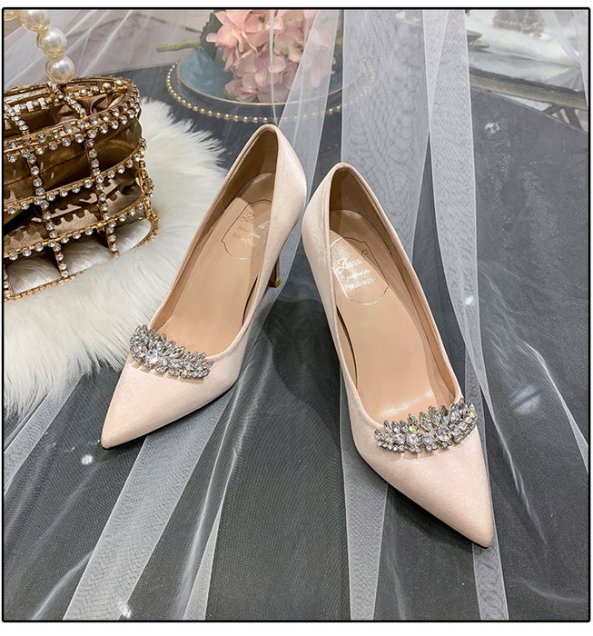 Pair of beige high-heeled shoes with crystal embellishments on a gray fabric background.