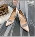 Pair of beige high-heeled shoes with crystal embellishments on a gray fabric background.