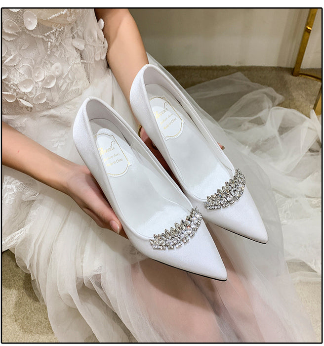 White wedding shoes with crystal embellishments held by a person in a white dress.