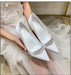 White wedding shoes with crystal embellishments held by a person in a white dress.