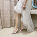 Person wearing a white dress and high heels in a room with a curtain and mirror.