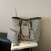 A tote bag with a brown leather trim and a matching zip pouch, both featuring a beige and blue geometric monogram pattern, displayed on a white book.
