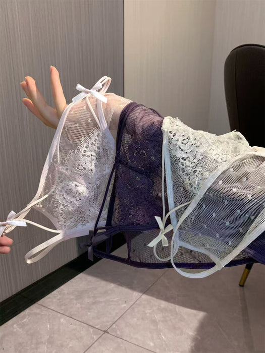 Three sheer lace and mesh lingerie pieces in white, dark purple, and pale blue-green are draped over a person's arm in an indoor setting.