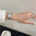 Hand wearing a silver watch with a plain background