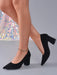 Black pointed-toe block-heel pumps worn on a model's feet, shown against a neutral gray background with a sparkly sequined fabric prop.