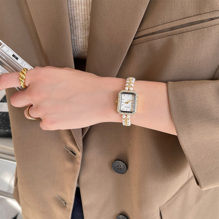 Person wearing a gold watch and ring, holding a phone, with a beige coat.