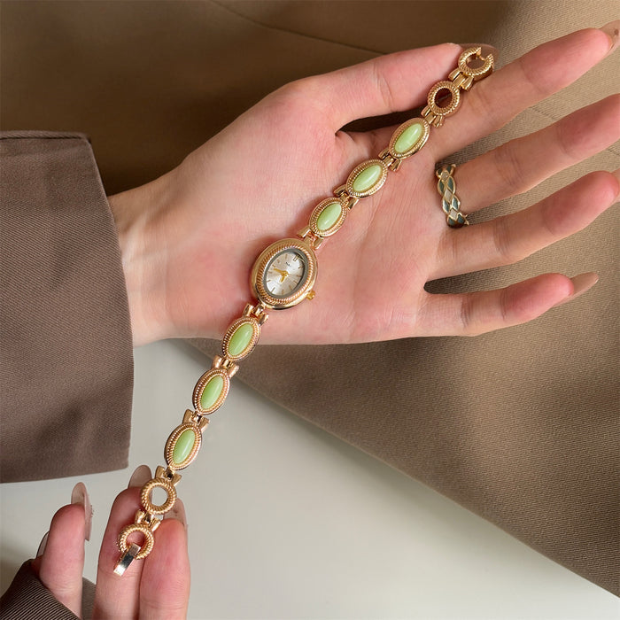 Gold bracelet with green gemstones on a hand against a beige background