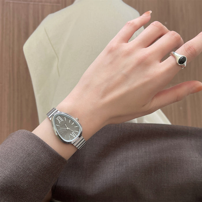 A close-up of a woman's hand wearing a silver-toned metal link watch with a gray dial and a silver signet ring with a black oval stone, set against a soft beige and brown background.